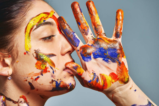Portrait of a beautiful girl in the paint. Closeup portrait of a girl with face and hands with different paint. Fashion art concept, beauty, creative people freelance people - Photo, Image