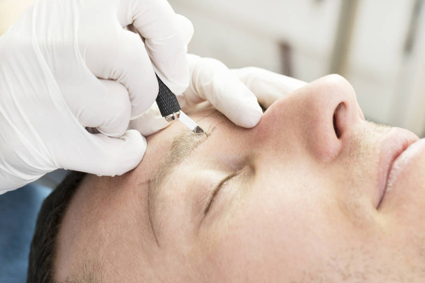 Young man microblading procedure to improve the condition of a mans eyebrows in a beauty salon. - Foto, Bild