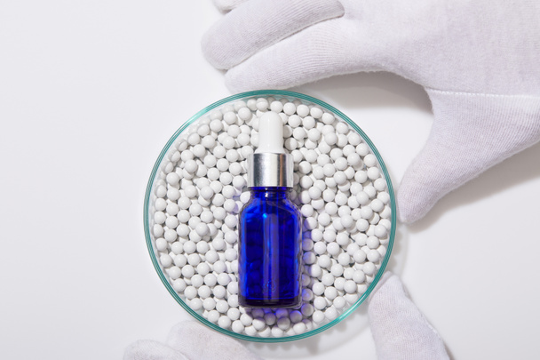 Обрезанный вид человека, держащего лабораторную стеклянную посуду с голубой бутылкой масла на декоративных бусах на белом фоне
 - Фото, изображение