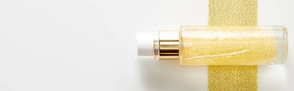 Vista dall'alto di bottiglia di olio cosmetico su striscia dorata su sfondo bianco, colpo panoramico
 - Foto, immagini