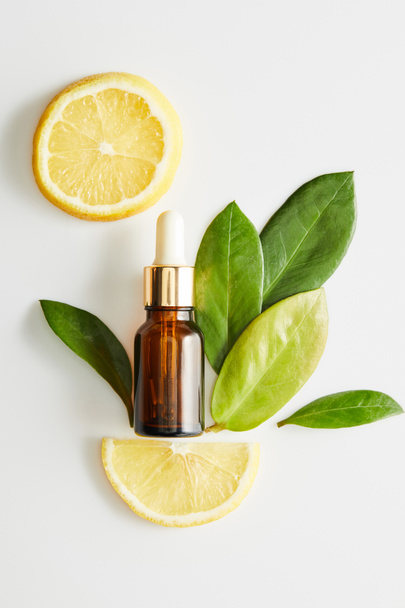 Draufsicht auf eine Flasche Kosmetiköl mit Blättern und Zitronenscheiben auf weißem Hintergrund - Foto, Bild