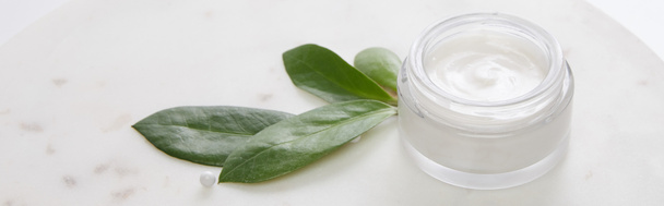 Crema cosmética con hojas y cuentas decorativas sobre fondo blanco, plano panorámico
 - Foto, Imagen