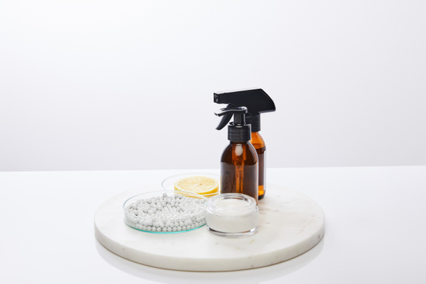 Bottles of oil, cosmetic cream and laboratory glassware with decorative beads, slice of lemon isolated on grey - Photo, Image