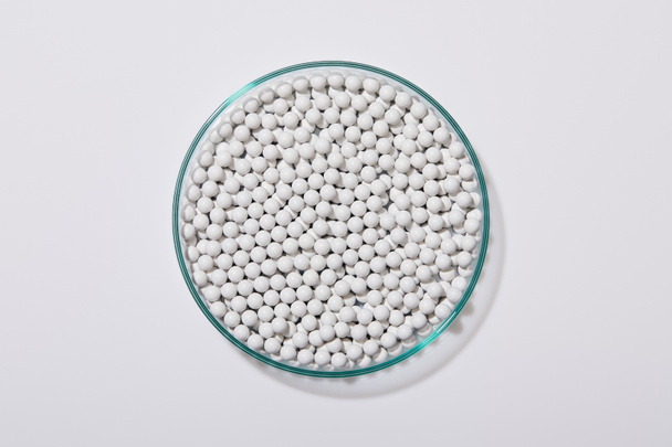 Top view of white decorative beads inside laboratory glassware on grey background - Foto, imagen