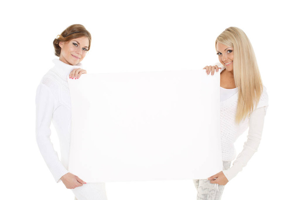 Two young pretty women in winter clothes with empty board for the text on a white background. - Foto, Imagen