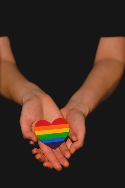 Female arms holding the heart coloured in LGBT pride colours on the dark background. Concept of the International Day Against Homophobia concept, sexual equality, feminism, social safety - Photo, Image