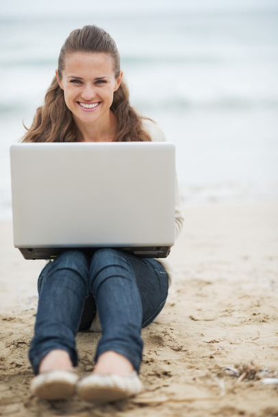 Woman in sweater sitting on beach with laptop - Foto, afbeelding