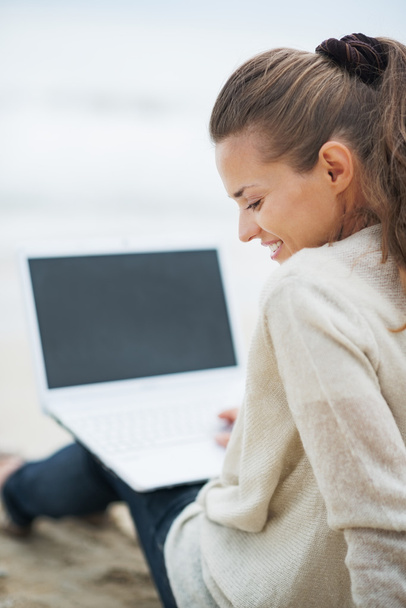 Woman in sweater sitting on beach with laptop - Valokuva, kuva