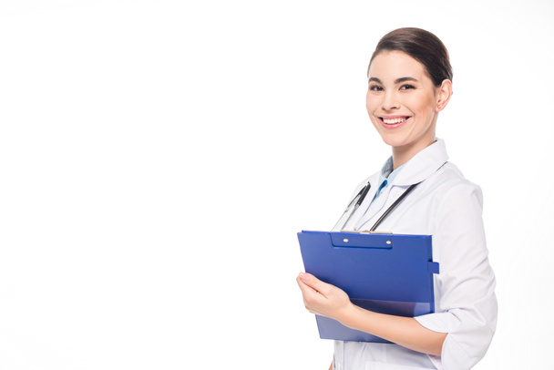 Prachtige lachende arts met stethoscoop en klembord kijken naar camera geïsoleerd op wit - Foto, afbeelding