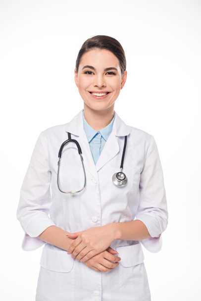 Attractive doctor in white coat and stethoscope smiling at camera isolated on white - Fotó, kép