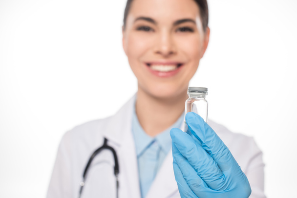 白色に隔離されたワクチンで瓶を保持する笑顔医師の選択的焦点 - 写真・画像