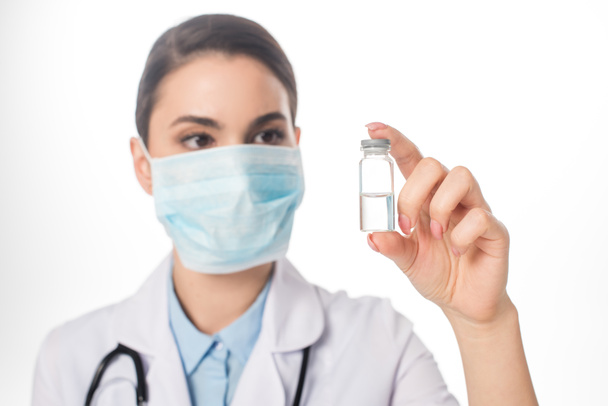 Selective focus of doctor in medical mask holding jar with vaccine isolated on white - Fotografie, Obrázek