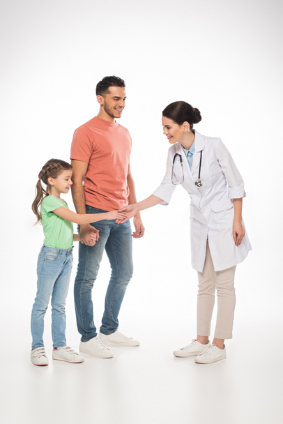 Full length of smiling pediatrician shaking hands with kid near father on white background  - Valokuva, kuva