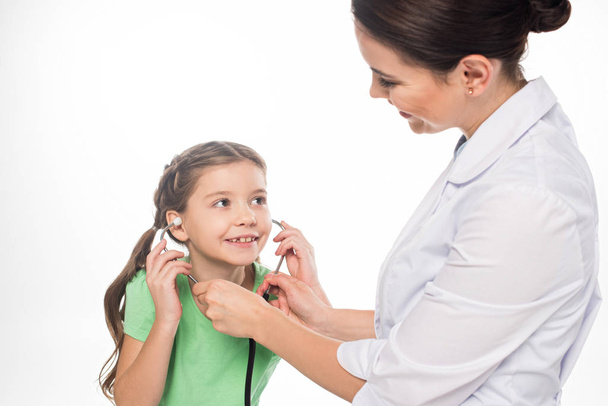 Uśmiechnięty pediatra daje stetoskop uśmiechniętemu dzieciakowi odizolowanemu na białym - Zdjęcie, obraz
