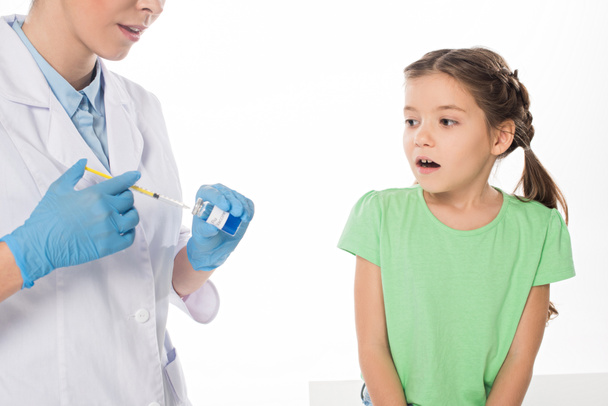 Pediatra zbierający szczepionkę przeciw grypie w strzykawce w pobliżu przestraszonego dziecka wyizolowanego na białym - Zdjęcie, obraz