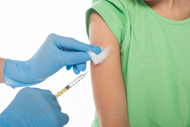 abgeschnittene Ansicht eines Kinderarztes, der Watte und Spritze hält, während er Impfstoff an ein Kind injiziert, das auf weiß isoliert ist - Foto, Bild