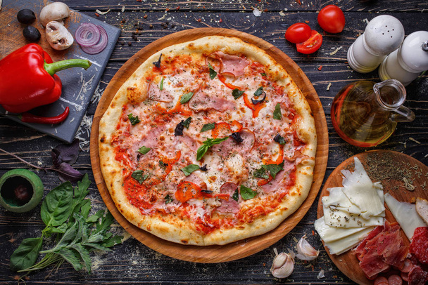 Top view of pizza with meat, tomatoes, cheese, basil on a wooden plate. Italy food. I - Fotó, kép