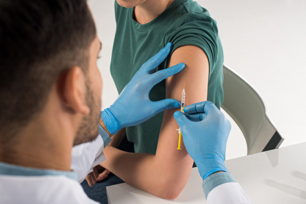 Selectieve focus van de arts die vaccininjectie geeft in de schouder van de patiënt geïsoleerd op wit - Foto, afbeelding