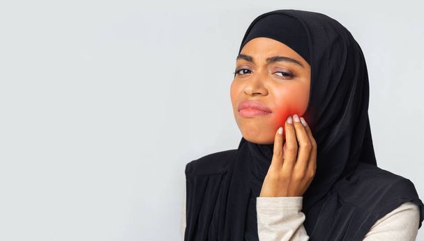 Μαύρο μουσουλμανικό κορίτσι έχει πονόδοντο, αγγίζοντας μάγουλο με κόκκινη φλεγμονή ζώνη - Φωτογραφία, εικόνα