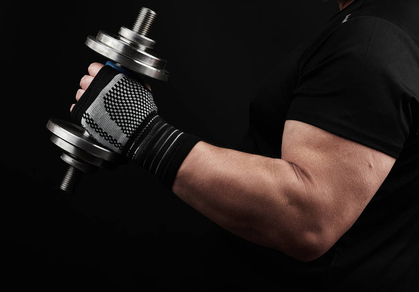 bodybuilder in a black uniform holds in his left hand a steel ty - Fotografie, Obrázek