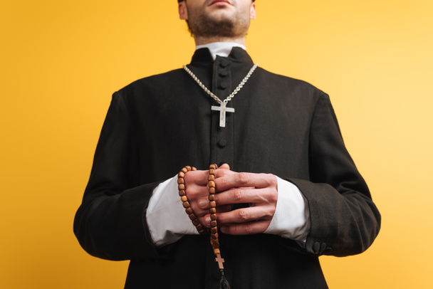 low angle view of catholic priest holding wooden rosary beads isolated on yellow - Fotoğraf, Görsel