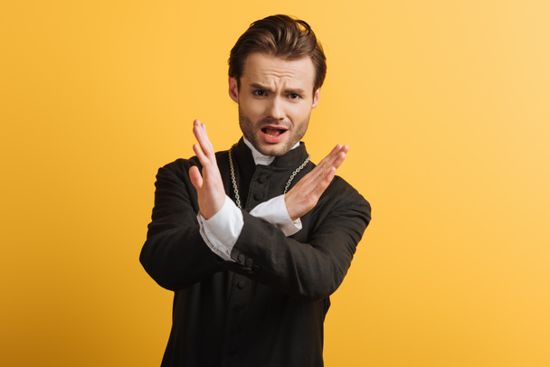 displeased catholic priest showing stop gesture and looking at camera isolated on yellow - Fotoğraf, Görsel