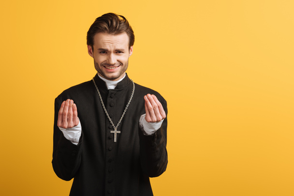 discouraged catholic priest showing question gesture isolated on yellow - 写真・画像
