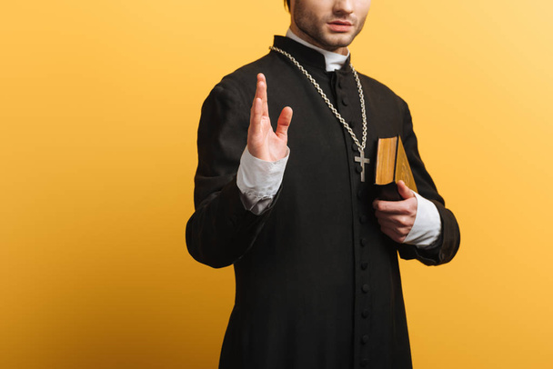 vista ritagliata del sacerdote cattolico che mostra gesto di benedizione mentre tiene la Bibbia isolata sul giallo
 - Foto, immagini