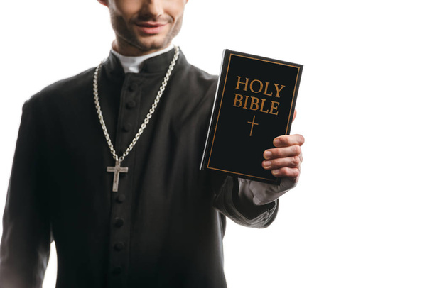 vista recortada del joven sacerdote católico que muestra la sagrada Biblia aislada en blanco
 - Foto, imagen