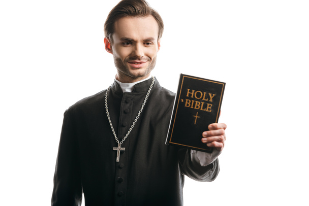 giovane prete cattolico sorridente mentre tiene la santa bibbia isolata sul bianco
 - Foto, immagini