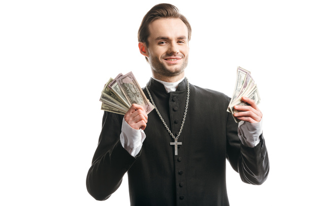 corrupt catholic priest smiling at camera while holding dollar banknotes isolated on white - Foto, Imagem