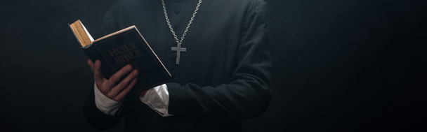 vue partielle du prêtre catholique lisant une bible sacrée isolée sur une photo panoramique noire
 - Photo, image