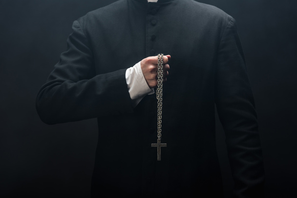 cropped view of catholic priest holding necklace with silver cross isolated on black - Fotó, kép