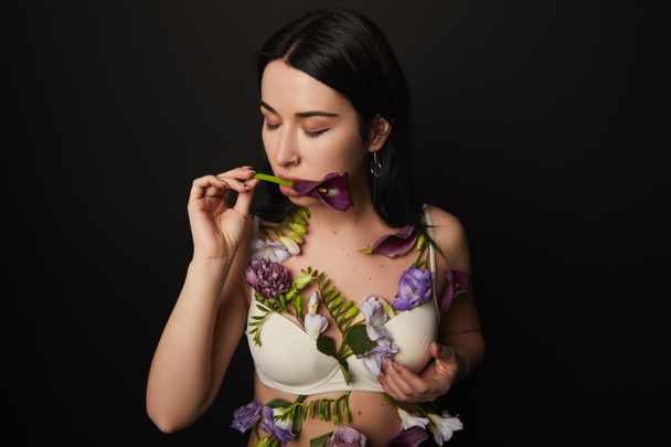 beautiful girl in bra with closed eyes and violet and purple flowers on body isolated on black - Photo, Image