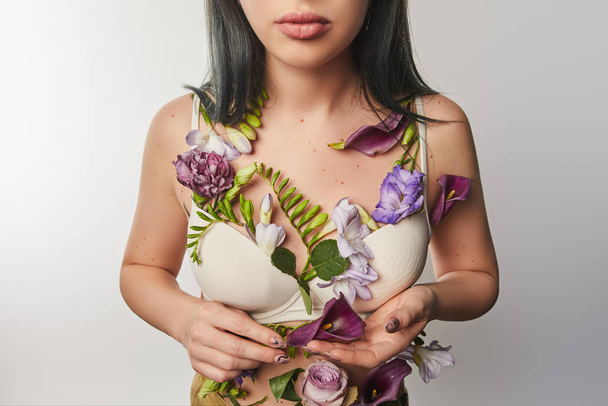 обрезанный вид девушки в бюстгальтере с фиолетовыми и фиолетовыми цветами на теле изолированы на белом
 - Фото, изображение