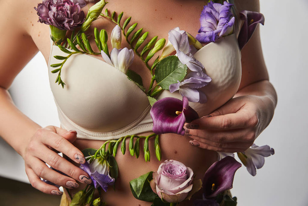 przycięty widok dziewczyny w biustonosz z fioletowymi i fioletowymi kwiatami na ciele odizolowany na białym - Zdjęcie, obraz