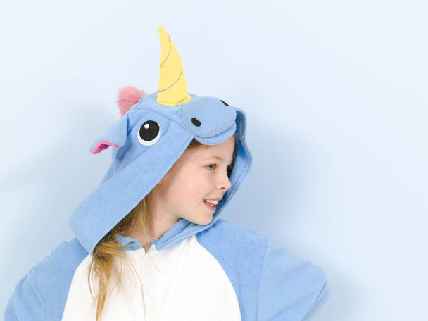happy pretty blonde girl in cozy unicorn costume in studio on blue background  - Photo, image