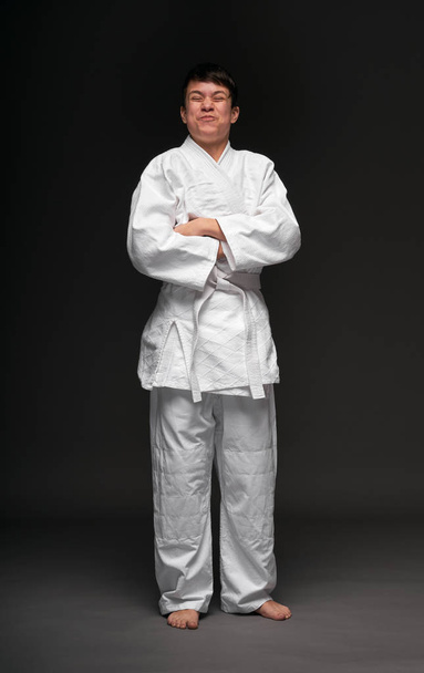 een tiener gekleed in vechtsport kleding poseert op een donkergrijze achtergrond, een sport concept - Foto, afbeelding