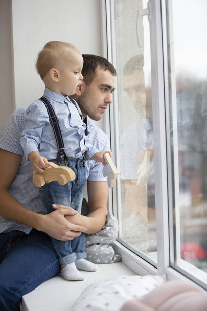 Vader en zoontje kijken uit het raam. Een man speelt met een kind. - Foto, afbeelding