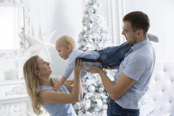 Famiglia a Natale. Madre padre e figlio giocano sullo sfondo di un albero di Natale. Genitori e figlio nel nuovo anno
. - Foto, immagini