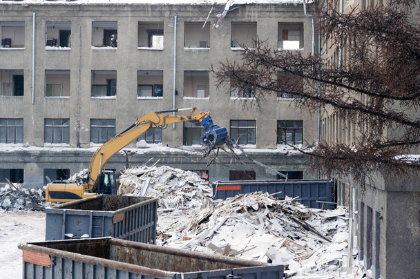 Monikerroksisen rakennuksen purkaminen, tuhoaminen suuren kaivinkoneen avulla
 - Valokuva, kuva