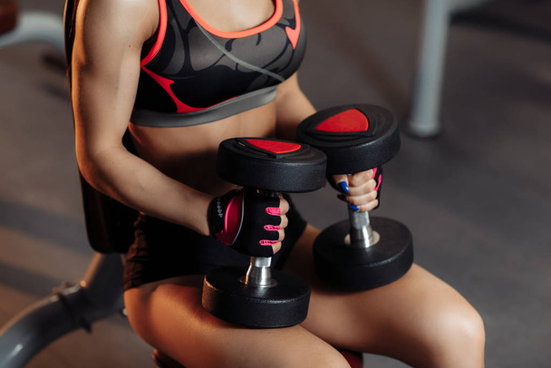 Close-up photo of young sporty woman preparing for exercises with dumbbells for shoulders on the bench in gym. - Valokuva, kuva