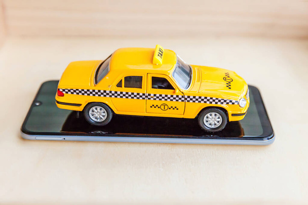 Smartphone aplikacji taxi do wyszukiwania online połączeń i koncepcji kabiny rezerwacji. Wystarczy zaprojektować żółty samochód zabawka Taksówka na pusty ekran smartfona na drewnianym tle. Symbol taksówki. - Zdjęcie, obraz