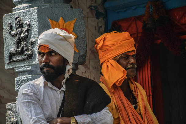 Archivfoto von 40 bis 60 Jahre alten indischen Priestern, die weiße und safranfarbene Tücher und Turban tragen, in der Nähe der Säule des Tempels von Mailapur, Karnataka.  - Foto, Bild