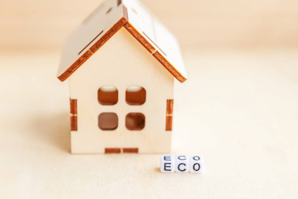 Miniature toy model house with inscription ECO letters word on wooden backdrop. Eco Village, abstract environmental background. Ecology zero waste social responsibility recycle bio home concept - Photo, Image