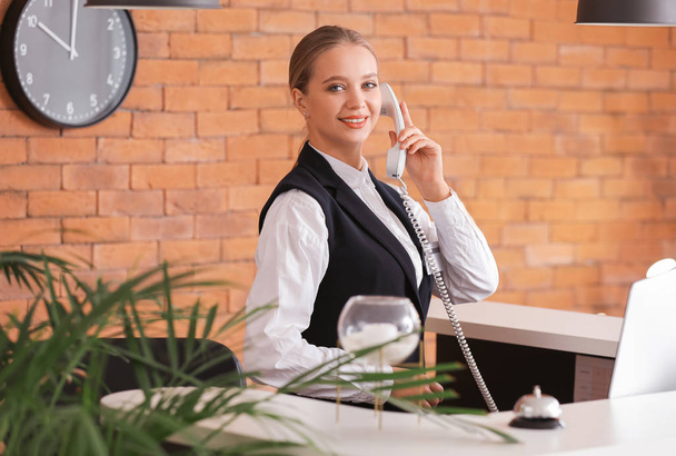 Young female receptionist talking by telephone at desk in hotel - Photo, Image