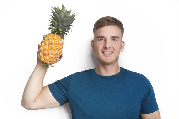 Handsome happy guy, young beautiful man holding fresh ripe fruit, yellow tropical pineapple in hand, smiling isolated on white background. Healthy diet, food, vegan or vegetarian. Love fruits concept - Foto, afbeelding