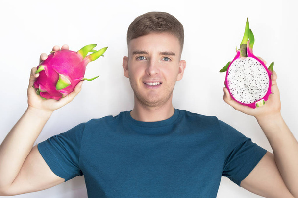 Dragon fruit. Beauty, healthy food, love fruits, vegan, vegetarian concept. Handsome happy guy, young beautiful man smiling, holds, keeps exotic tropical 2 two ripe pitaya, half, whole pitahaya cactus - Foto, afbeelding