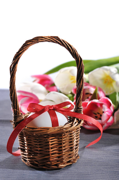 white easter egg with red bow in easter nest with tulips in the background  - Фото, зображення