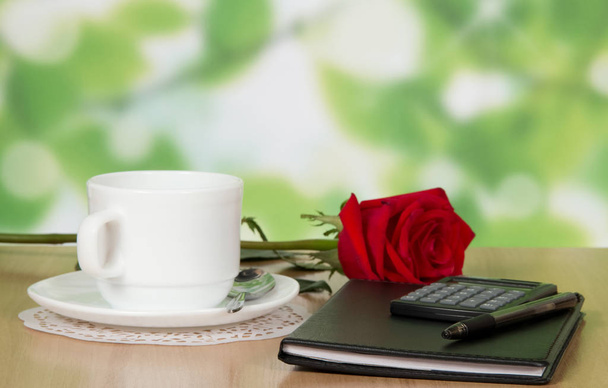 Office accessories, cup, saucer and a rose on the table - Photo, Image